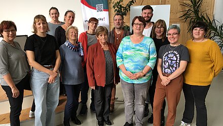 Gruppenfoto von Teilnehmenden in einem Seminarraum vor Banner und Pflanzen Gruppenfoto in einem Seminarraum